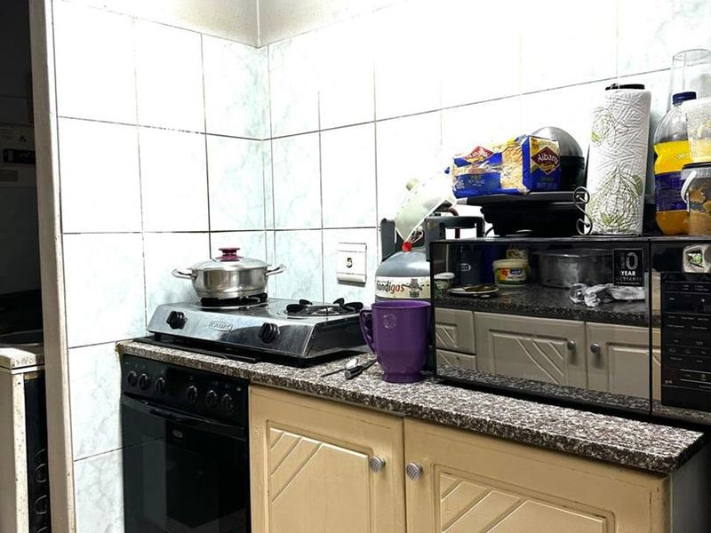 A compact kitchen featuring built-in cabinetry, a gas hob with oven, granite countertops, and tiled wall finishes.