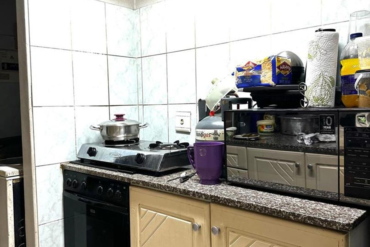 A compact kitchen featuring built-in cabinetry, a gas hob with oven, granite countertops, and tiled wall finishes.