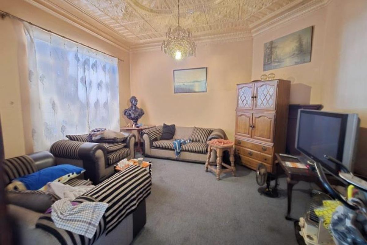 A living room featuring a decorative pressed metal ceiling, ornate chandelier, and large window, offering a traditional aesthetic with potential for modernization.