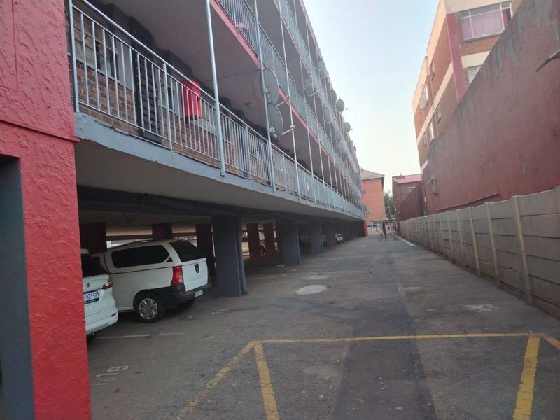 Exterior view of an apartment building featuring a covered ground-level parking area, concrete structural pillars, and a precast boundary wall.