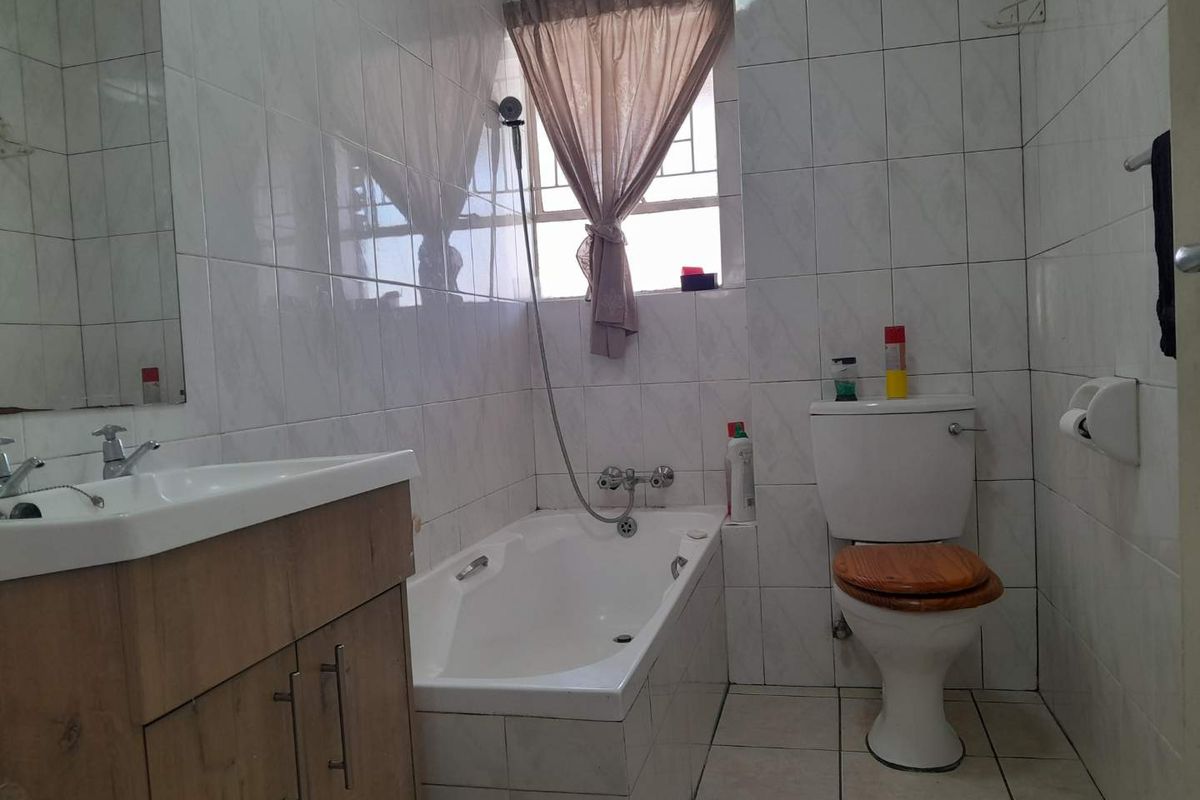 A functional bathroom featuring a built-in vanity, bathtub with shower mixer, and toilet, finished with full-height wall tiling and floor tiles.