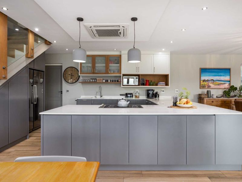 Modern open-plan kitchen featuring a large central island, stone countertops, integrated appliances, and sleek cabinetry, seamlessly connected to the living area and staircase.