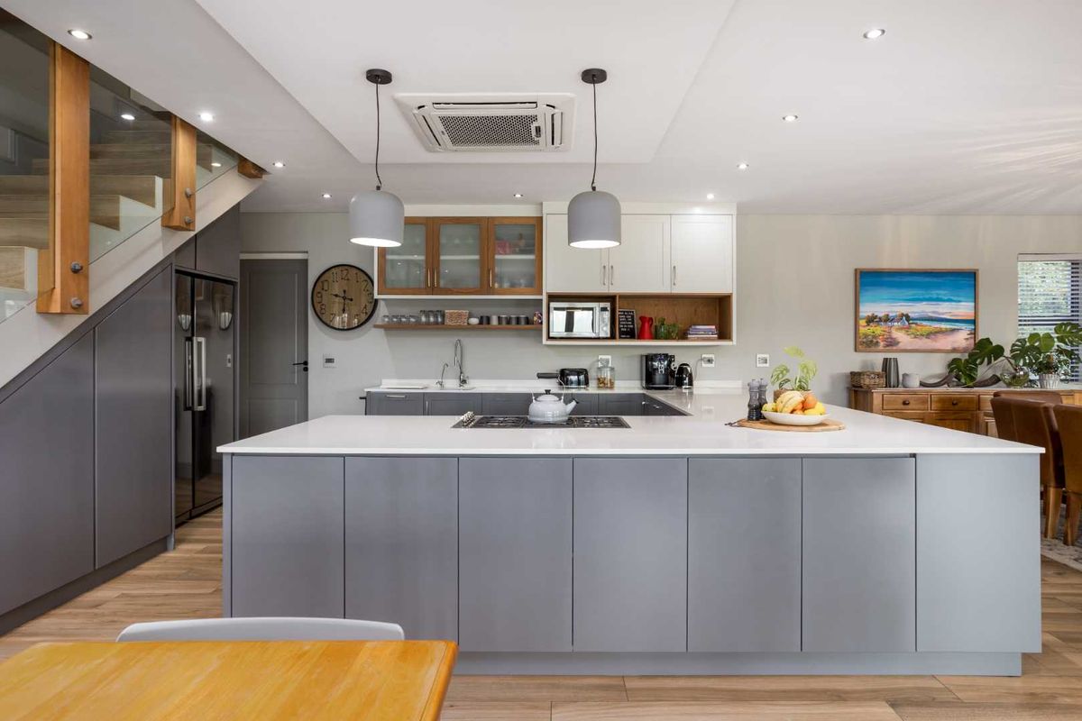 Modern open-plan kitchen featuring a large central island, stone countertops, integrated appliances, and sleek cabinetry, seamlessly connected to the living area and staircase.
