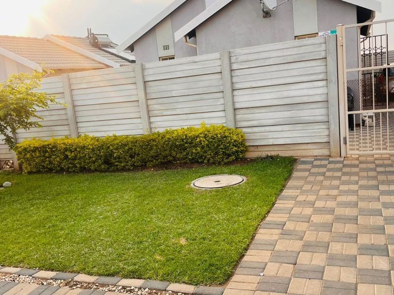 Front exterior view featuring a paved driveway, metal gate, and a precast concrete boundary wall with a landscaped lawn area.