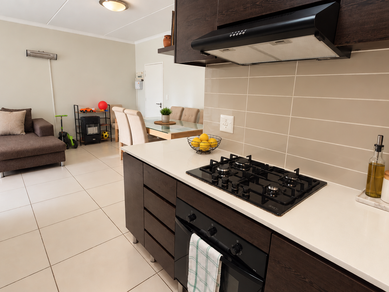 Modern open-plan living area featuring a contemporary kitchen with dark cabinetry, gas hob, extractor fan, and light quartz countertops flowing into the dining space.