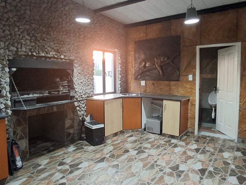 Covered entertainment area featuring a built-in braai, kitchenette with sink, and an attached restroom facility with a urinal.