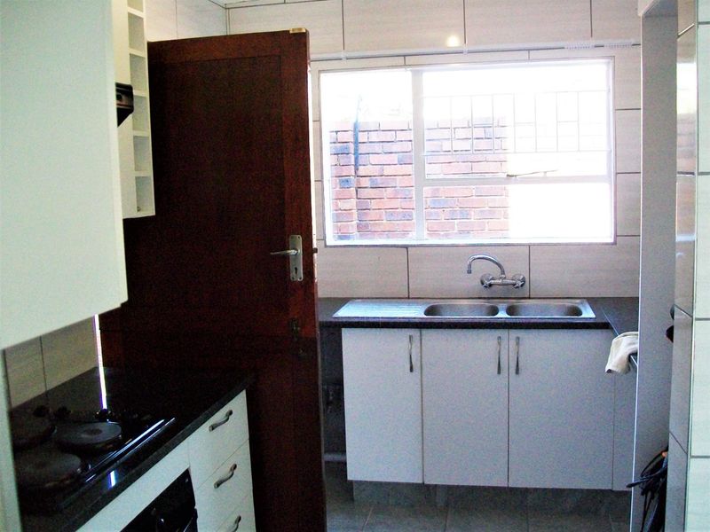 A functional kitchen featuring built-in cabinetry, a double sink, and a built-in oven and hob, with tiled finishes and natural light.