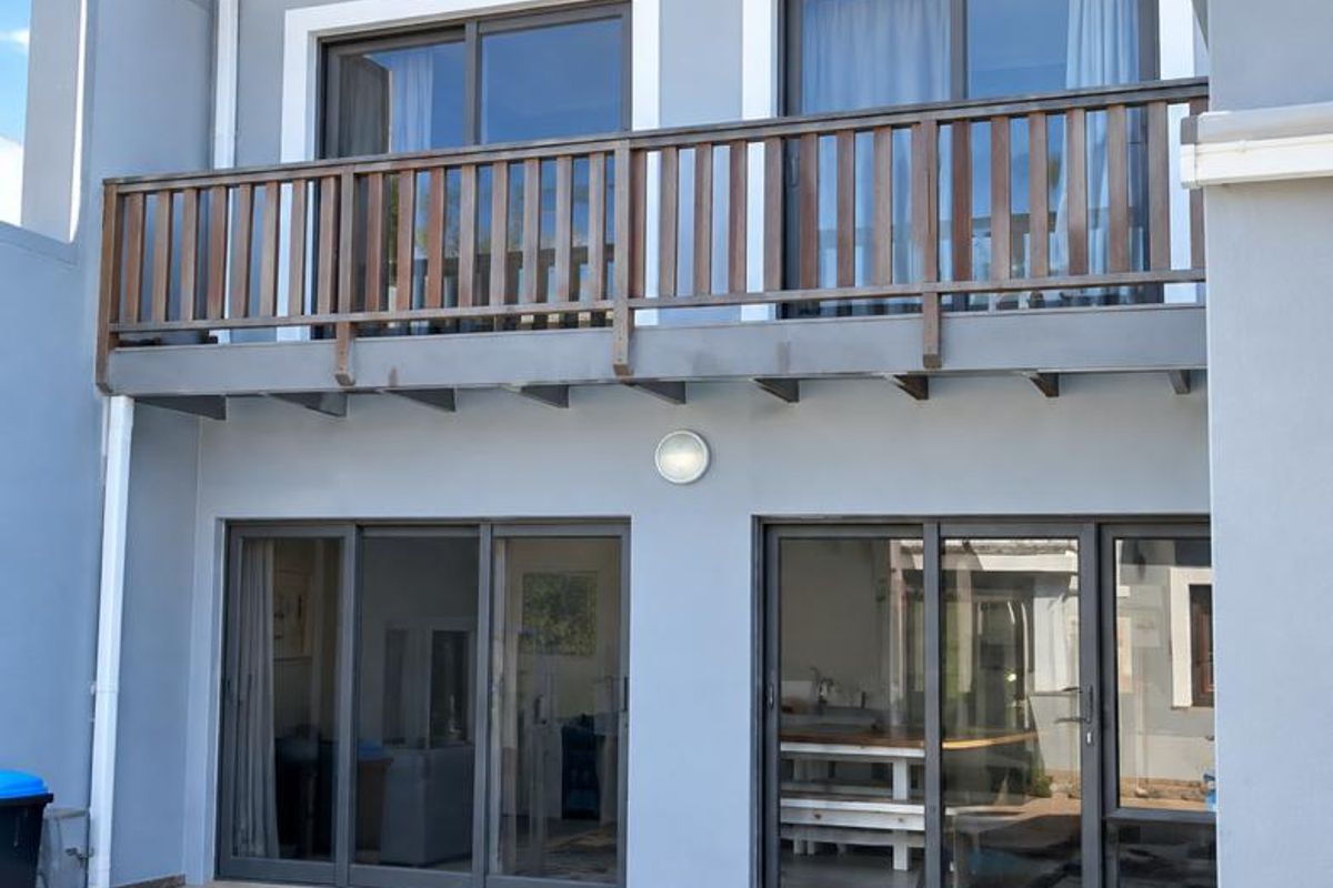 Rear view of the house featuring a swimming pool, paved deck, and a balcony with a wooden balustrade accessible via sliding glass doors.