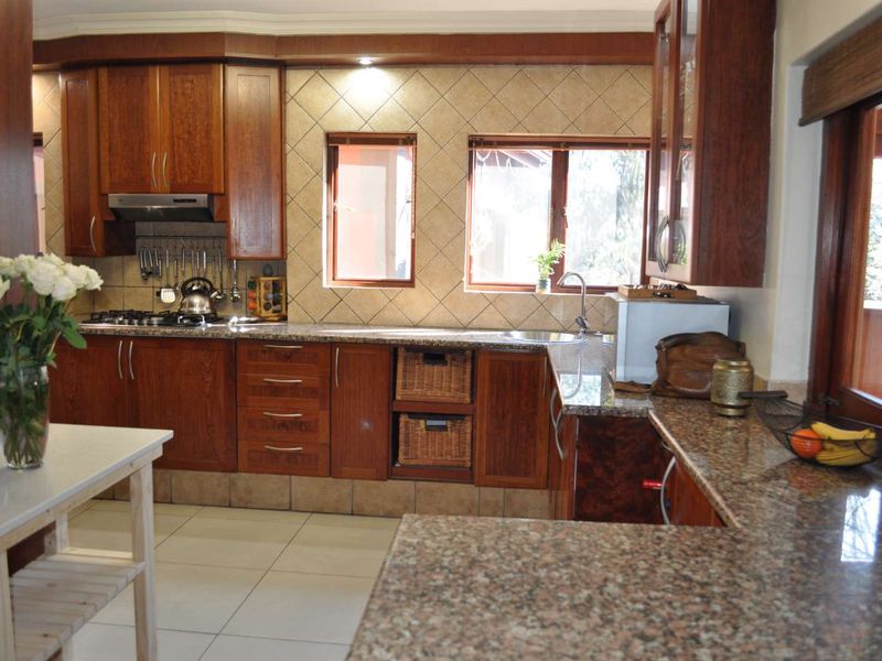 A functional kitchen featuring warm-toned wooden cabinetry, granite countertops, a gas hob with extractor fan, and a tiled backsplash with dual windows.