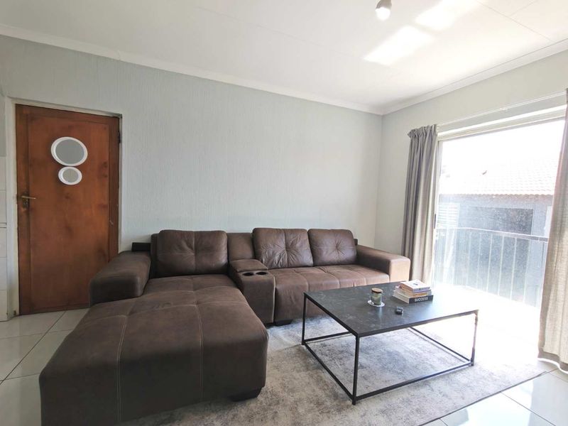 A bright living room featuring tiled flooring and a sliding glass door providing access to a balcony.