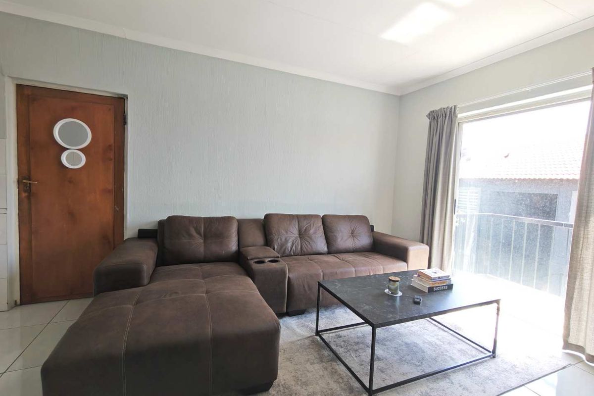 A bright living room featuring tiled flooring and a sliding glass door providing access to a balcony.