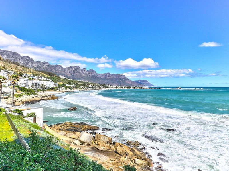 A stunning panoramic coastal view featuring the Atlantic Ocean, rocky shoreline, and the iconic Twelve Apostles mountain range in the background.