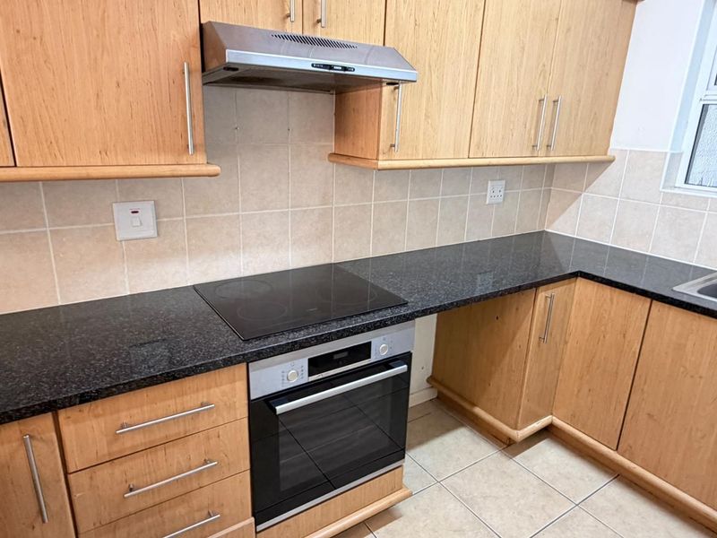 A functional kitchen featuring light wood cabinetry, dark granite countertops, a built-in oven, electric hob, and a stainless steel extractor fan.