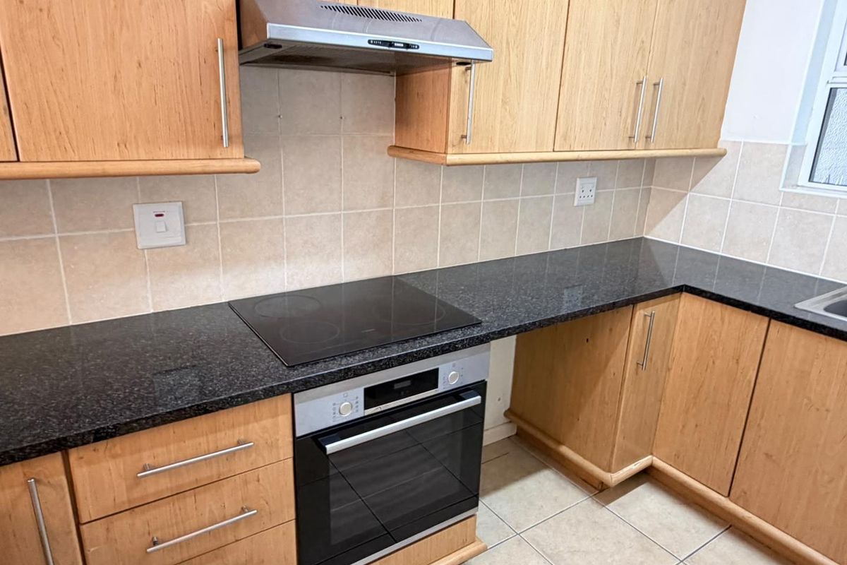 A functional kitchen featuring light wood cabinetry, dark granite countertops, a built-in oven, electric hob, and a stainless steel extractor fan.