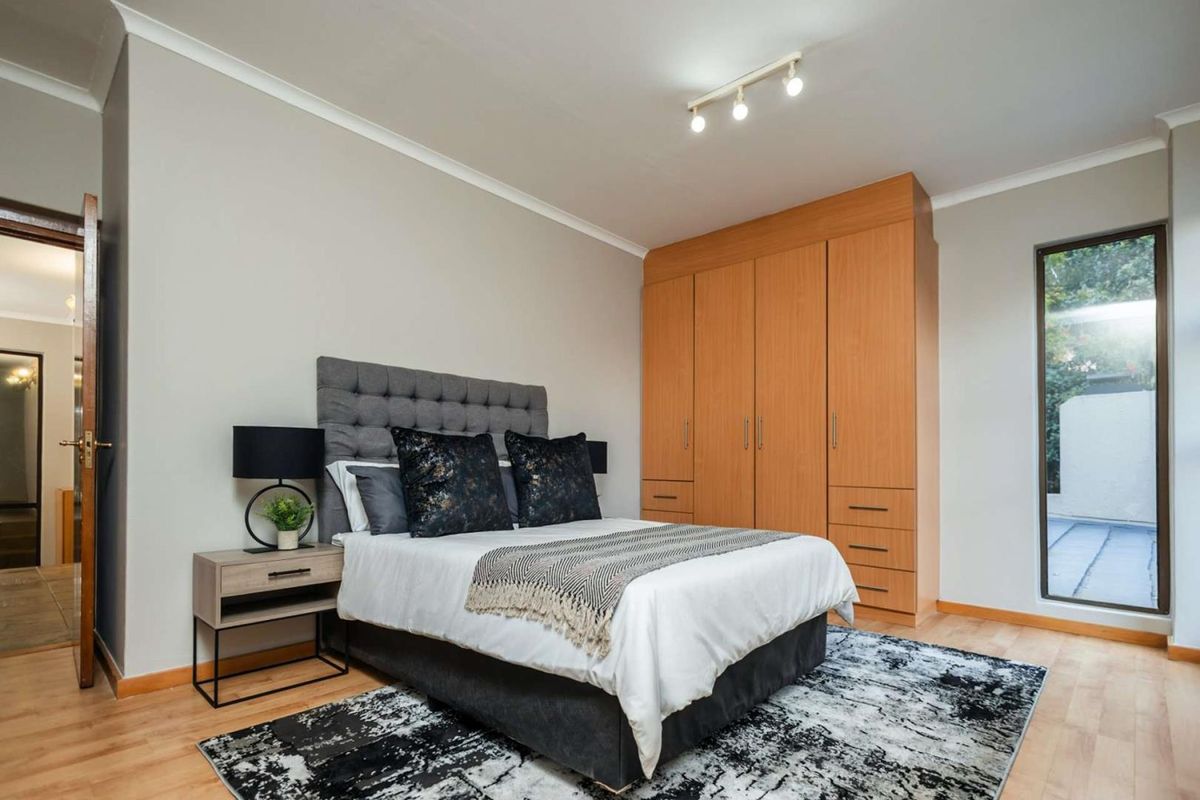 A well-maintained bedroom featuring built-in wooden cabinetry, laminate flooring, and a vertical window providing natural light.