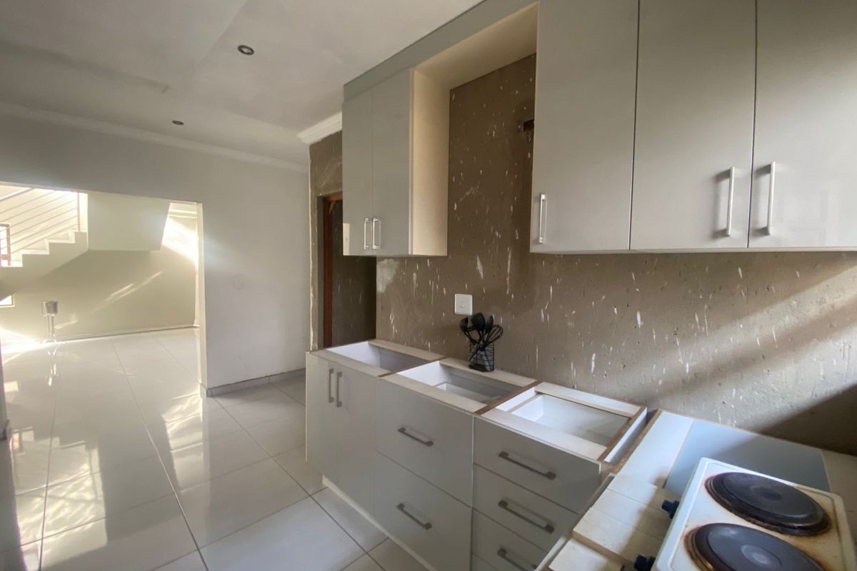 An unfinished kitchen area featuring installed cabinetry, tiled flooring, and an electric hob, requiring completion of the splashback and countertop installation.