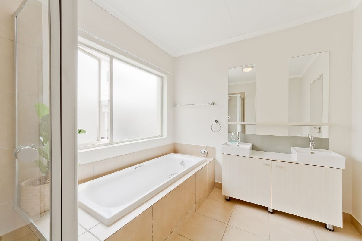 A bright and clean bathroom featuring a built-in bathtub, a double vanity with twin sinks, and a separate shower enclosure with tiled flooring.