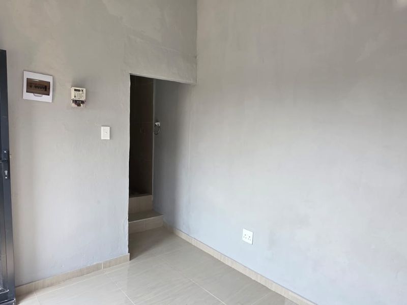 An empty, unfinished living area featuring tiled flooring, exposed plaster walls, and integrated electrical infrastructure, ready for final finishes and interior design.