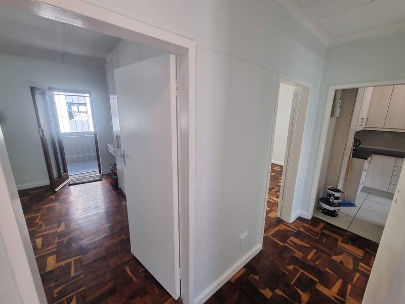 A bright hallway featuring classic parquet flooring, providing access to the kitchen area and an exterior entrance with a security gate.