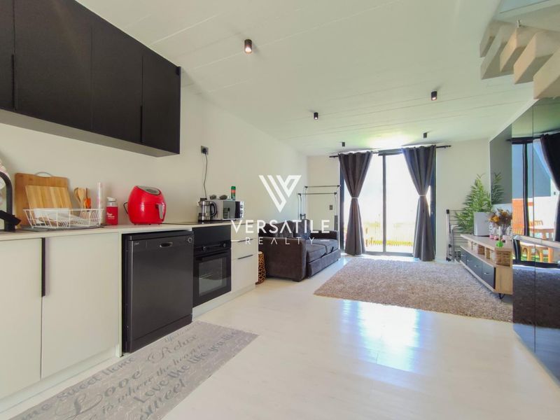 Modern open-plan living area featuring a sleek kitchen with built-in cabinetry and oven, flowing seamlessly to a bright lounge with sliding door access.