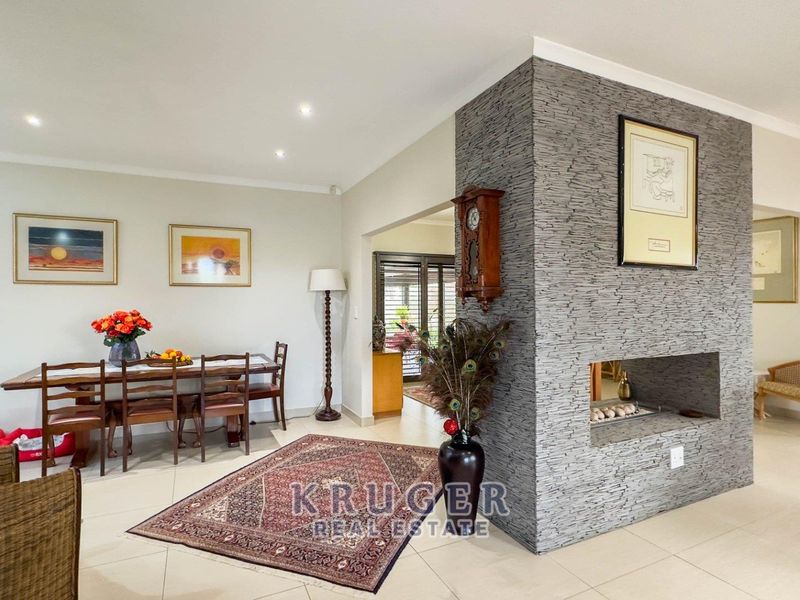 Spacious open-plan living and dining area featuring a modern stone-clad central fireplace and neutral tiled flooring throughout.