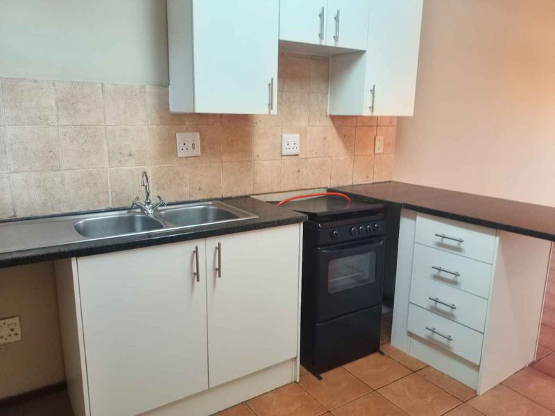 A functional kitchen featuring white cabinetry, dark laminate countertops, a double bowl sink, and a freestanding stove with tiled splashbacks and flooring.