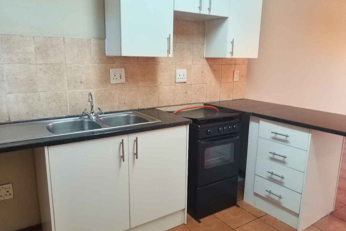 A functional kitchen featuring white cabinetry, dark laminate countertops, a double bowl sink, and a freestanding stove with tiled splashbacks and flooring.