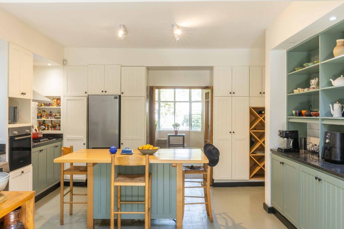 A well-appointed kitchen featuring sage green cabinetry, white pantry cupboards, a central island, and integrated storage with a view to the exterior.