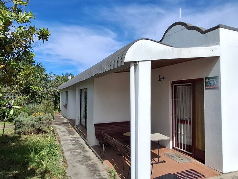 Front exterior view of the house featuring a covered patio, paved driveway, and established garden area with a concrete walkway.