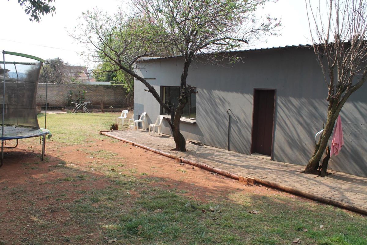 Rear view of the property featuring a paved walkway, exterior wall, and a spacious garden area with a brick boundary wall.