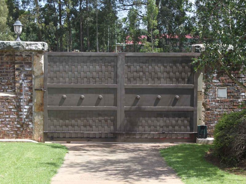 A secure entrance featuring a decorative metal driveway gate flanked by rustic brick boundary walls and stone pillar accents.