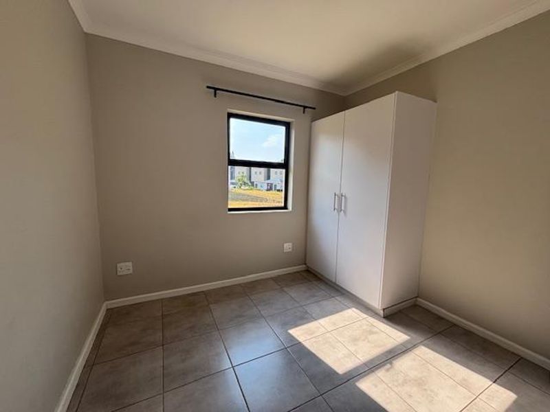 A clean, empty bedroom featuring neutral wall paint, tiled flooring, and a built-in white wardrobe.