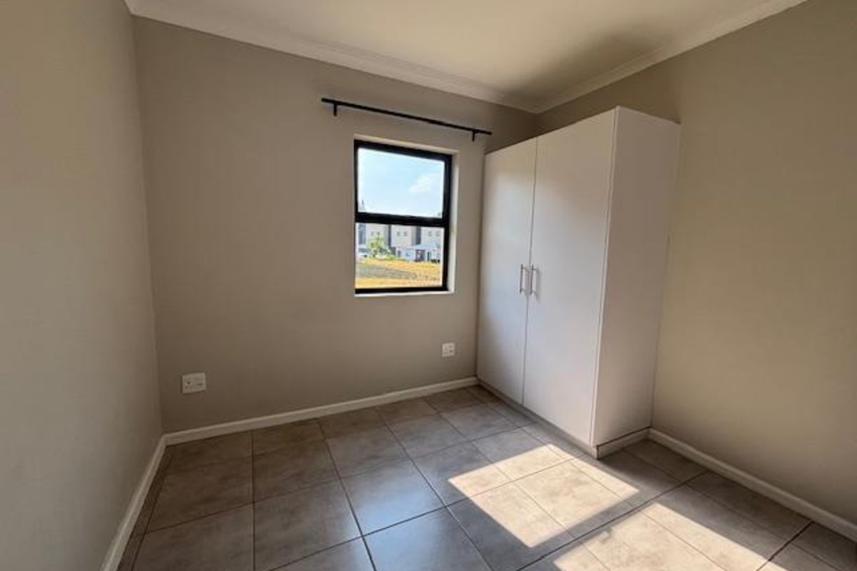 A clean, empty bedroom featuring neutral wall paint, tiled flooring, and a built-in white wardrobe.