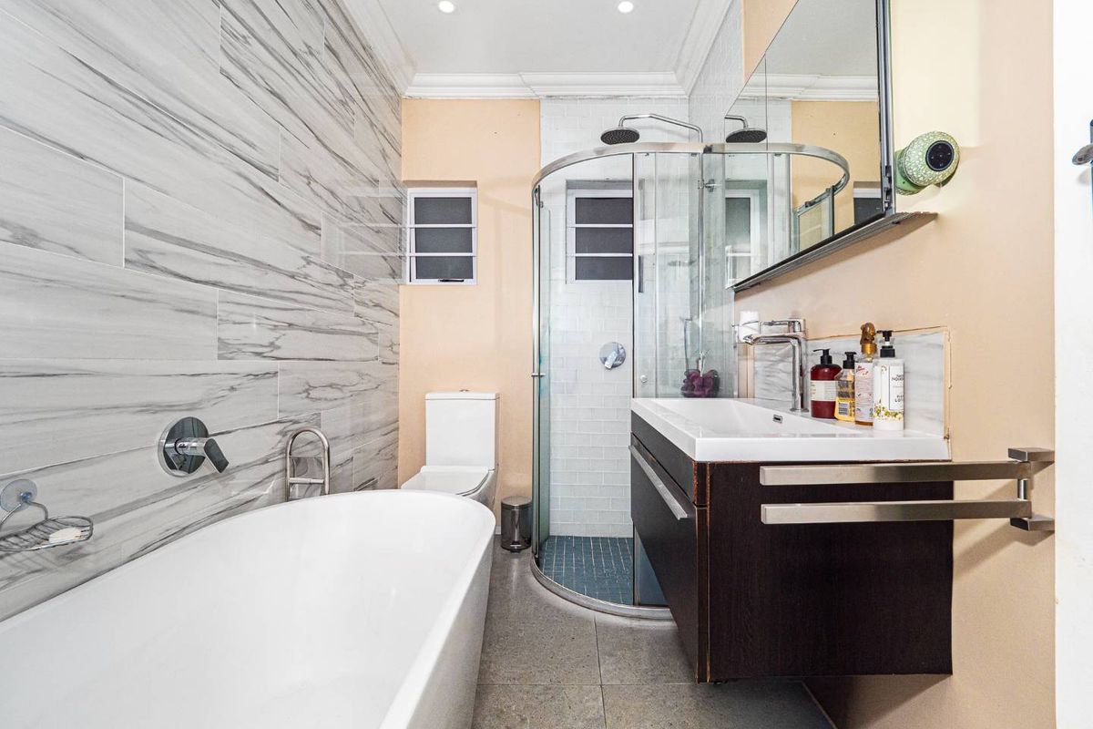 Modern bathroom featuring a freestanding bathtub, glass-enclosed corner shower, wall-mounted vanity, and contemporary marble-effect wall tiling.