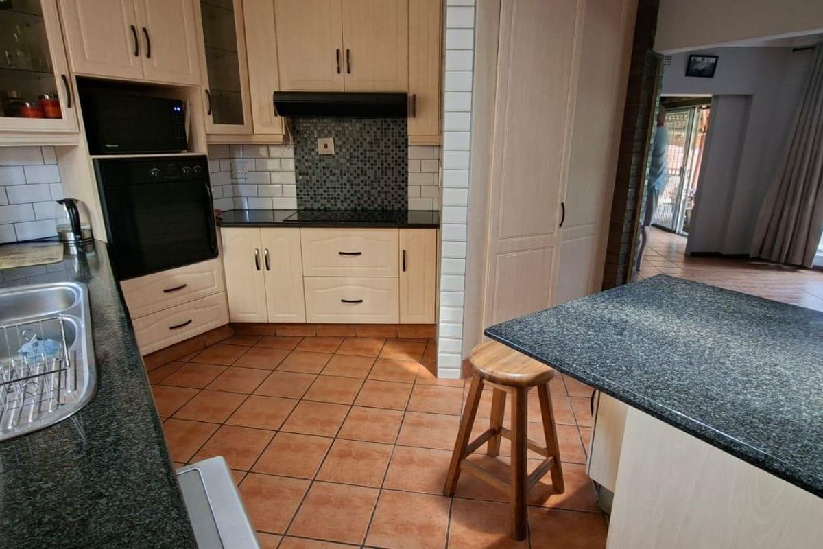 A functional kitchen featuring light wood cabinetry, granite countertops, a built-in oven, and a mosaic tile backsplash, with an adjacent open-plan living area.