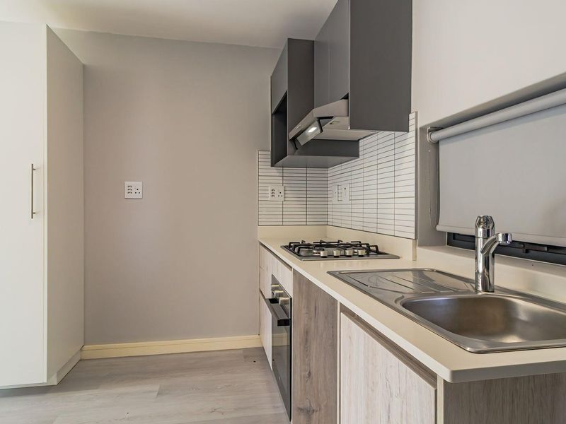 A modern, compact kitchen featuring built-in cabinetry, a gas hob, extractor fan, stainless steel sink, and tiled splashback in a clean, neutral finish.