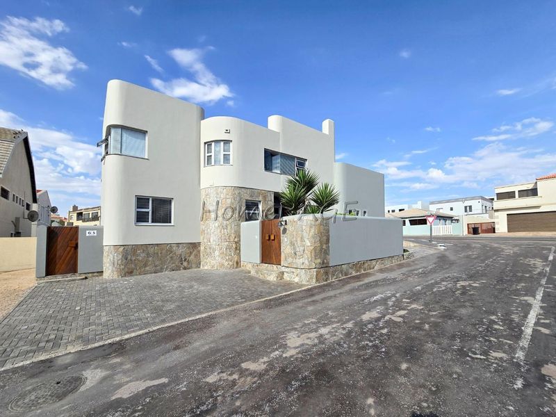 Modern architectural house exterior featuring curved walls, stone cladding, and a paved driveway with secure gated entrance.