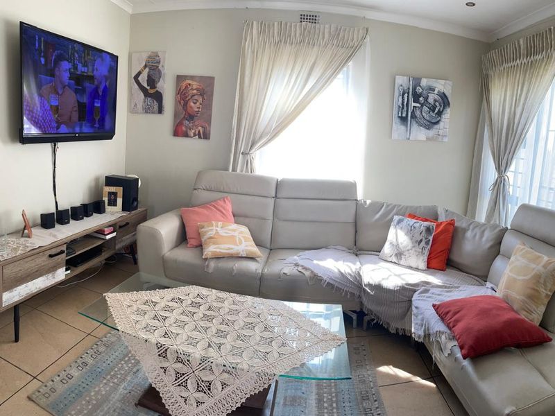 A comfortable living room featuring tiled flooring, neutral wall tones, and natural light through large windows with fitted curtain tracks.