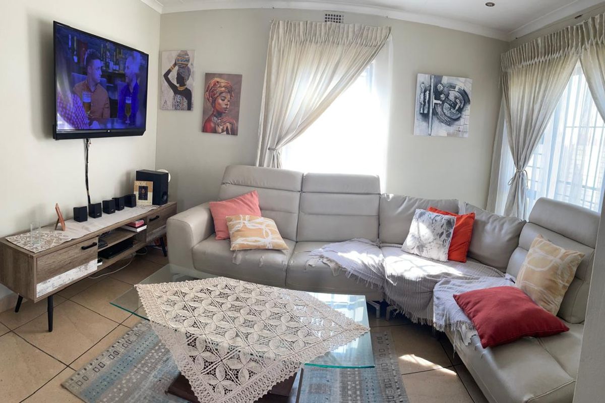A comfortable living room featuring tiled flooring, neutral wall tones, and natural light through large windows with fitted curtain tracks.