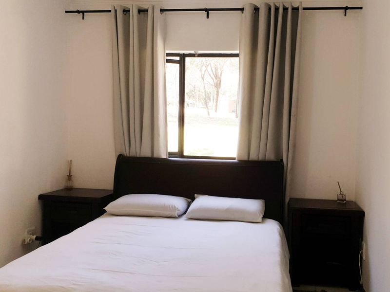 A simple bedroom featuring a window with a curtain rod, providing natural light and a view of the outdoors.