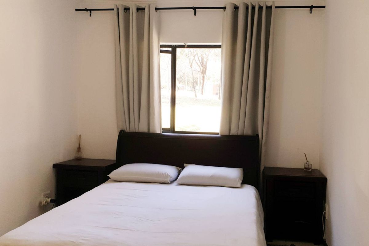 A simple bedroom featuring a window with a curtain rod, providing natural light and a view of the outdoors.