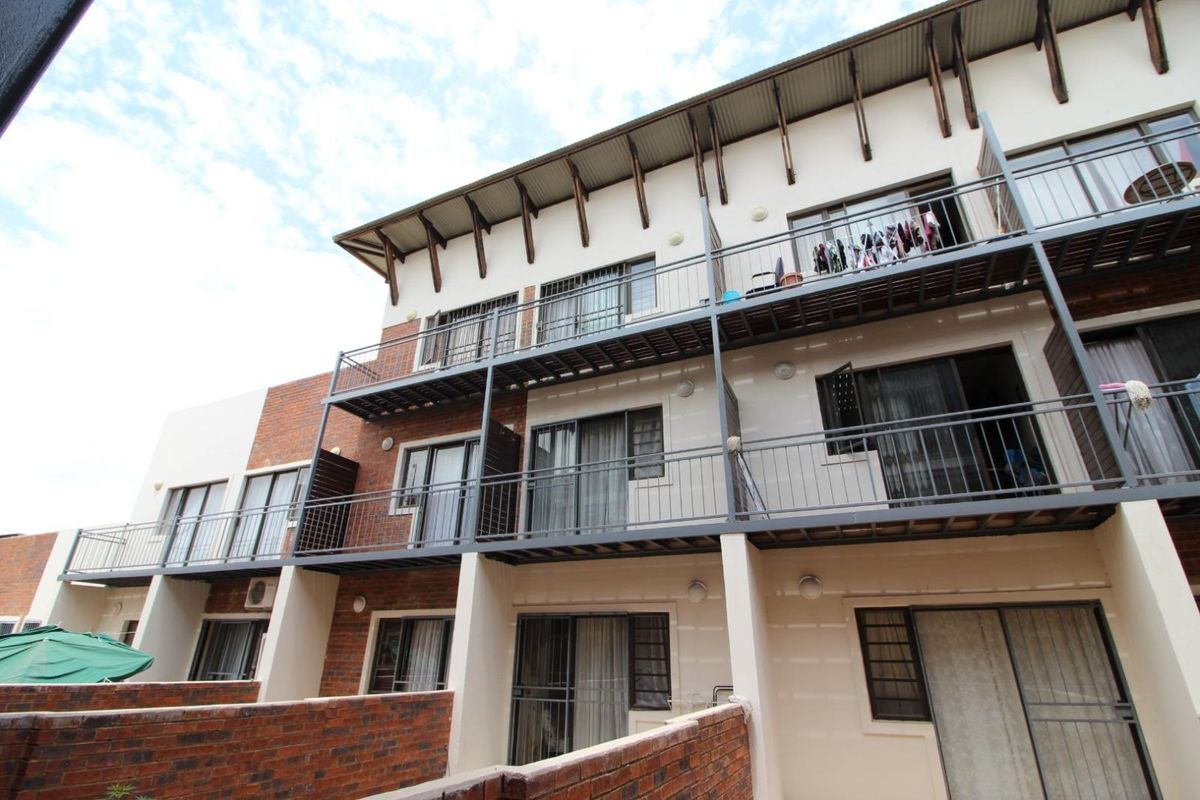 Exterior view of a multi-story apartment complex featuring brick and plaster facade, metal balcony railings, and sliding glass doors.