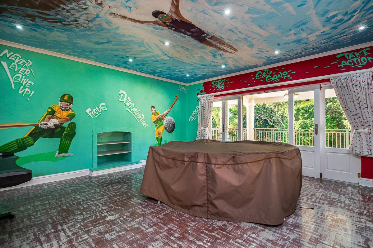 A versatile room featuring custom sports-themed wall and ceiling murals, recessed lighting, and double doors opening onto a covered balcony.