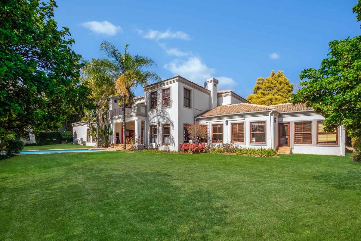 Spacious rear exterior view of the house featuring a well-maintained lawn, swimming pool, and a multi-level facade with a balcony.