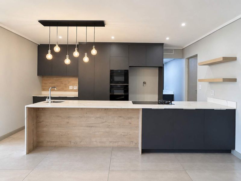 Modern kitchen featuring dark cabinetry, a large island with stone countertops, built-in appliances, and stylish pendant lighting in an open-plan layout.