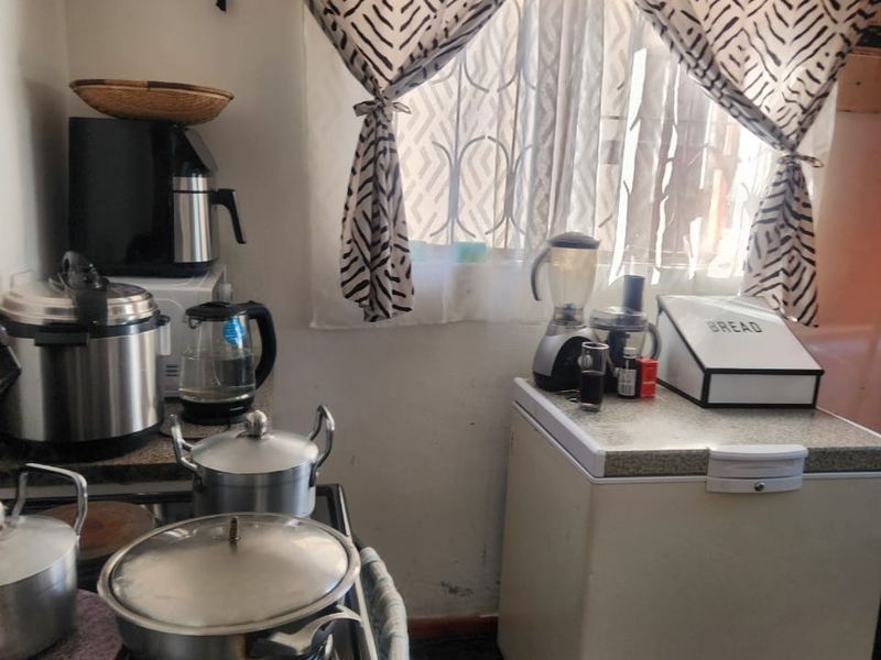 A compact kitchen area featuring dark tiled flooring, an electric stove, and a ventilation grille, currently showing signs of wear on the lower walls.