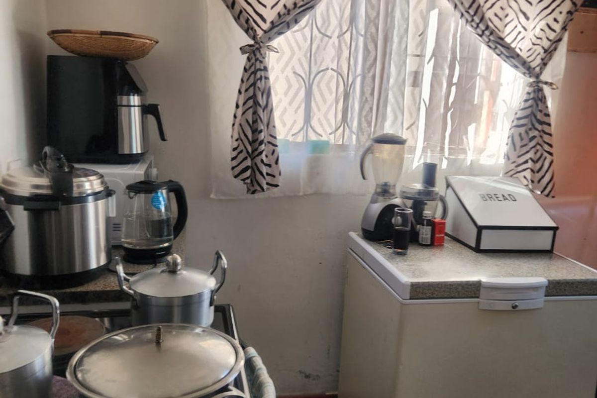 A compact kitchen area featuring dark tiled flooring, an electric stove, and a ventilation grille, currently showing signs of wear on the lower walls.