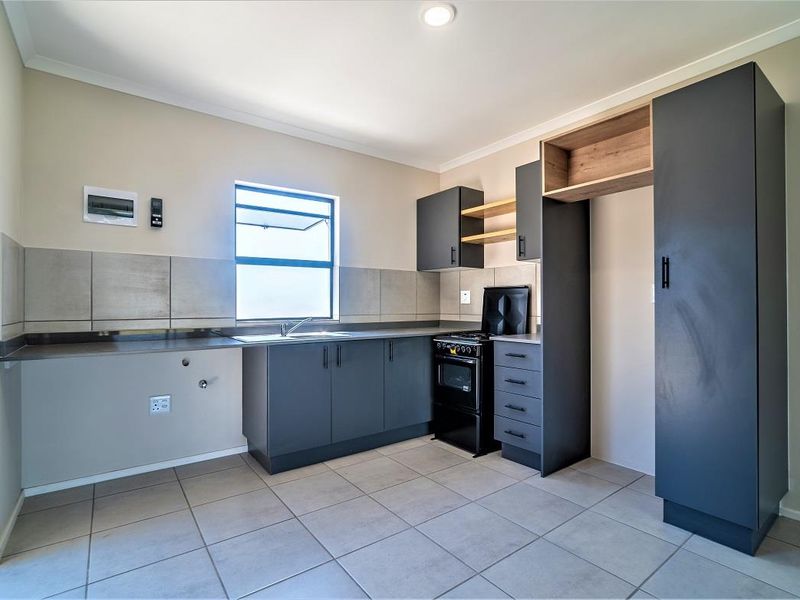 Modern kitchen featuring dark grey cabinetry, tiled flooring, a built-in sink, and a freestanding stove, offering a clean and functional workspace.