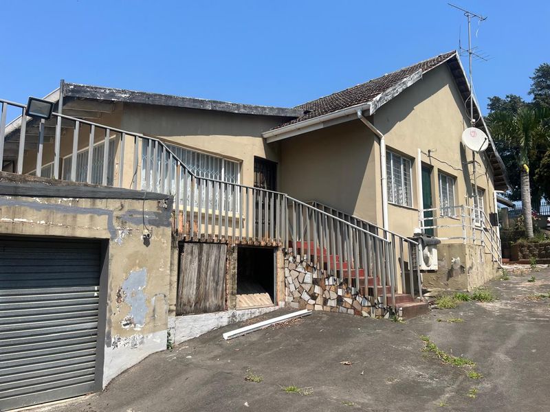 Rear exterior view of the house showing a metal staircase, garage access, and significant wear to the exterior wall finishes and structural elements.