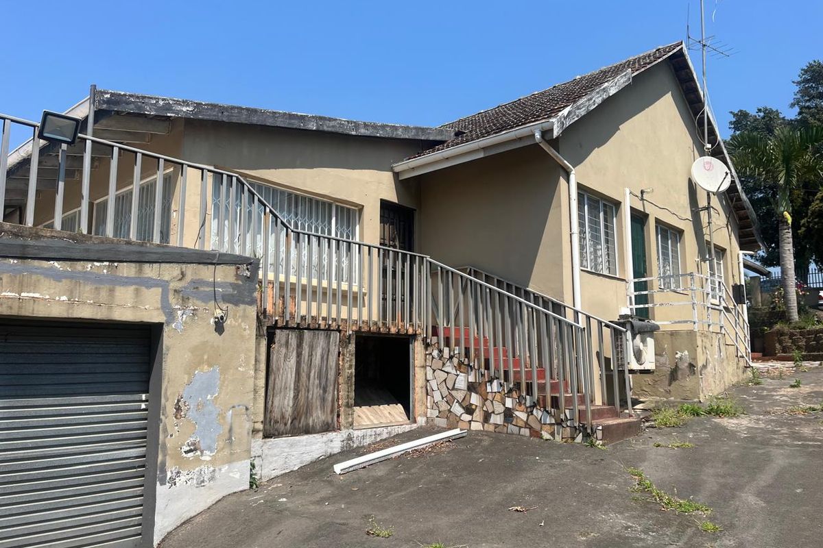 Rear exterior view of the house showing a metal staircase, garage access, and significant wear to the exterior wall finishes and structural elements.